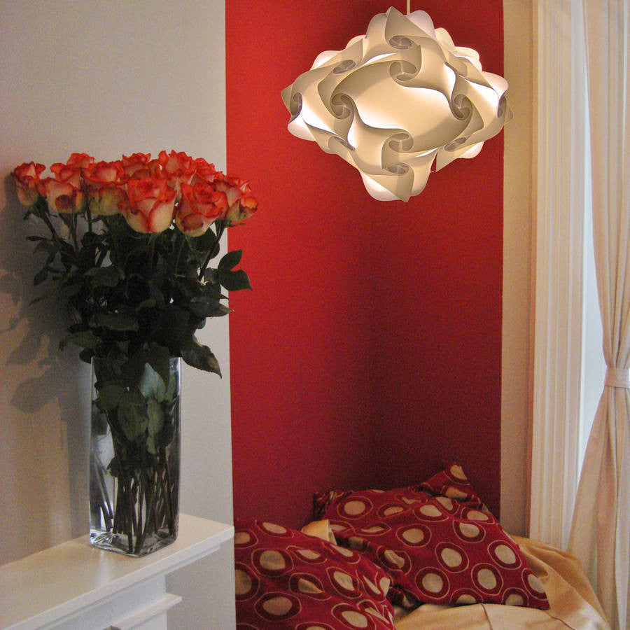 Stylish ceiling light shade in a modern, geometric design above a vase of vibrant red roses and a patterned throw pillow in a cozy, home interior setting.