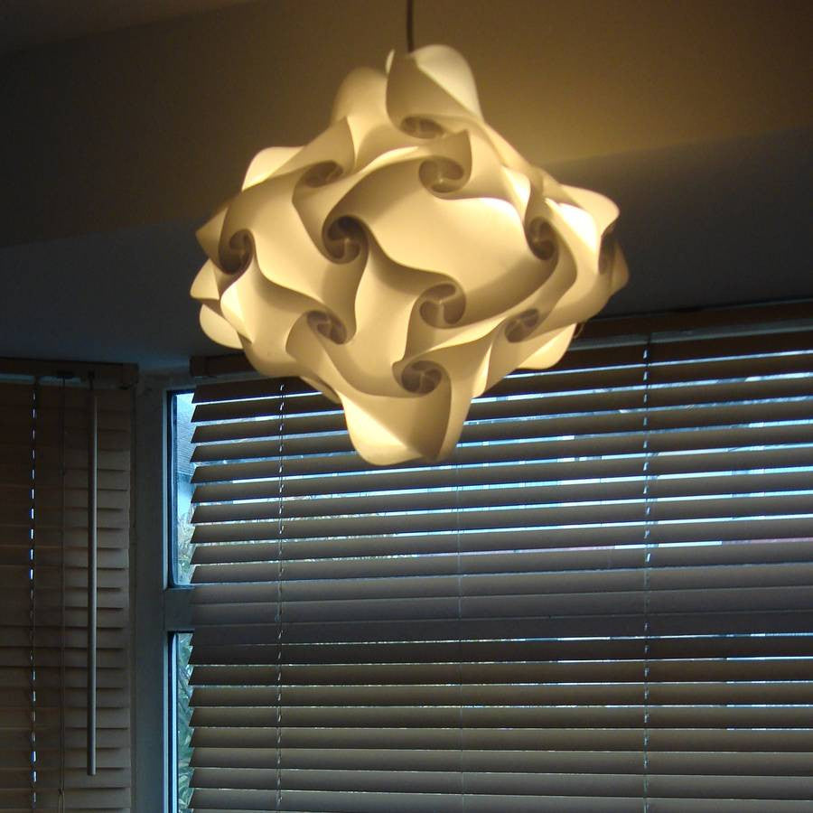 Elegant white geometric pendant lamp with a sculptural, swirling design suspending above a window with horizontal blinds.