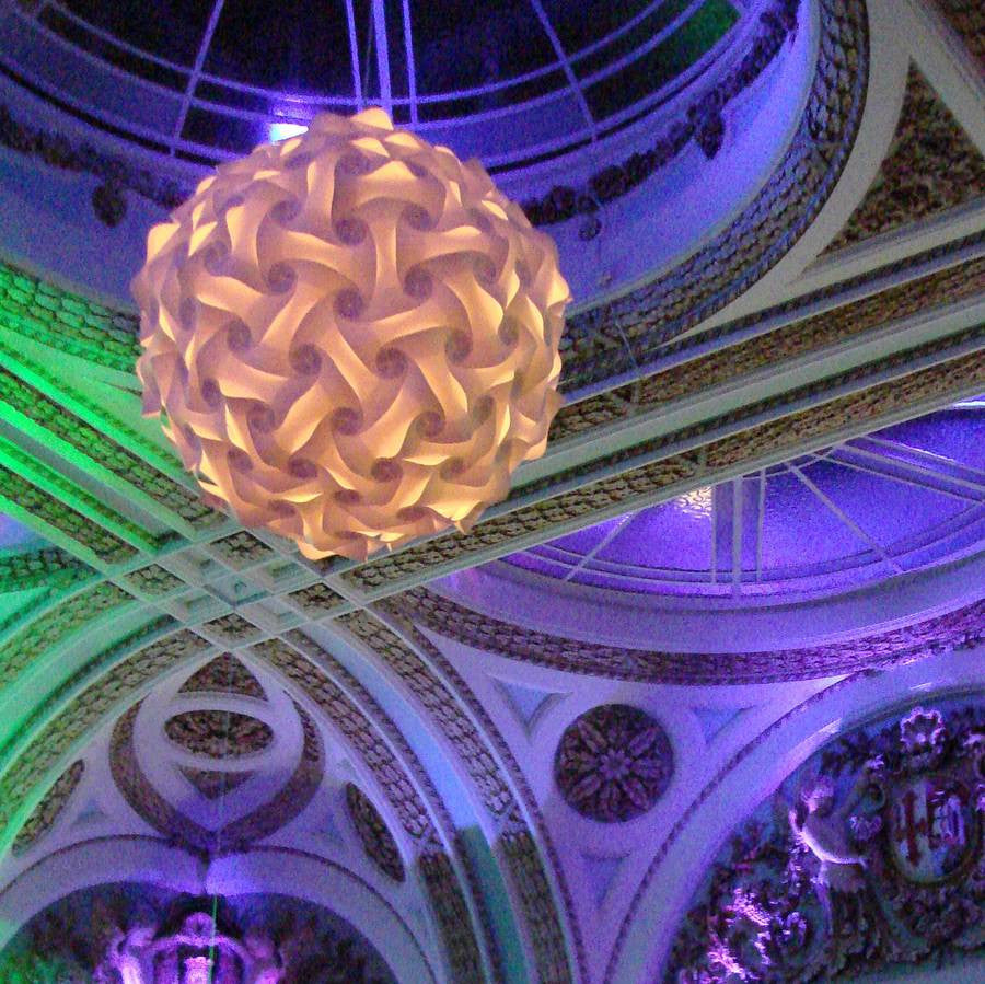 Intricate spherical lampshade suspended in ornate architectural interior with vibrant purple and green lighting.