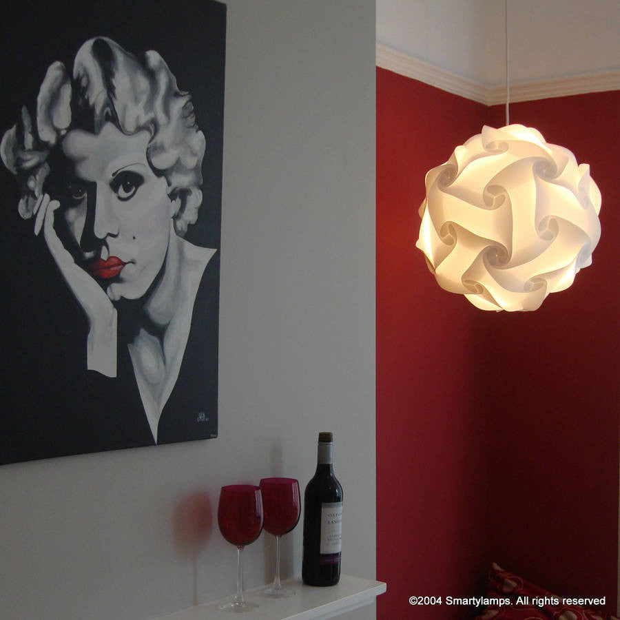Elegant modern lamp with pleated white shade hanging in a room with a red accent wall and a framed black and white portrait painting.