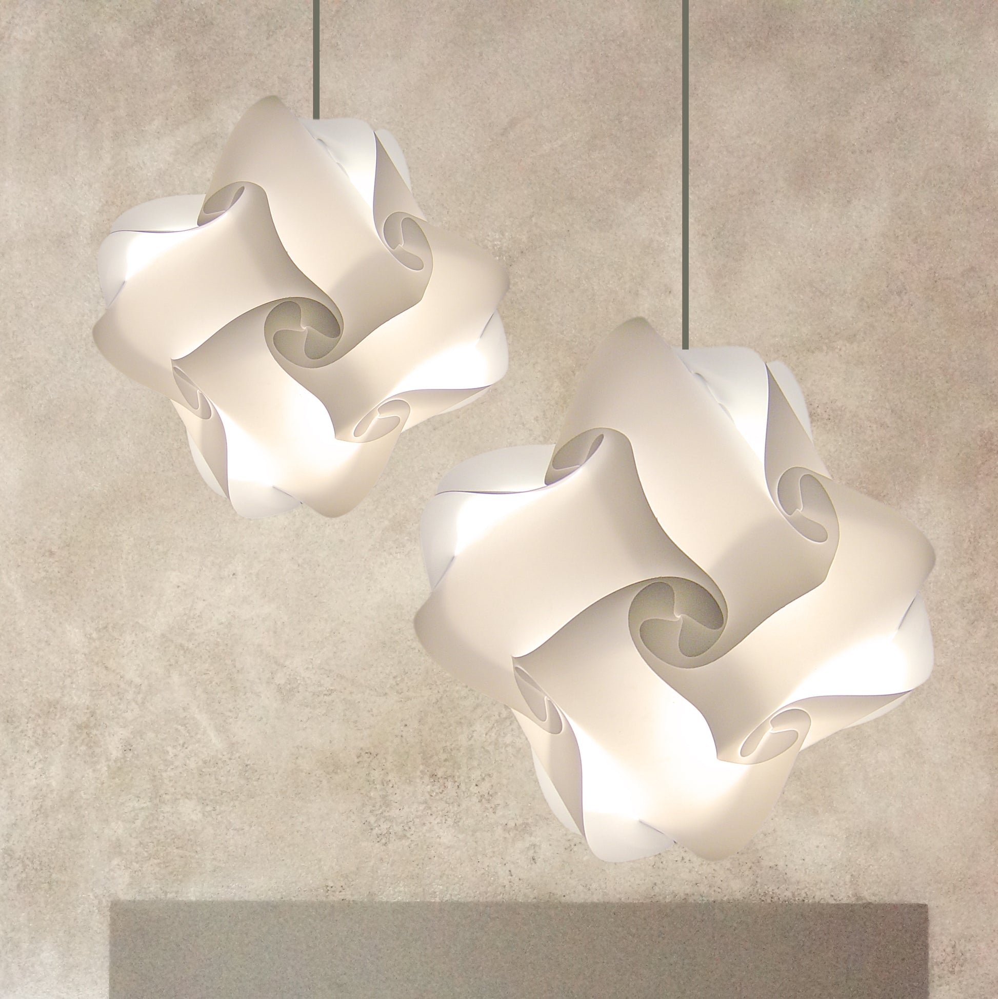 Elegant white pendant lamps with intricate swirling patterns, suspended from a minimalist gray background.