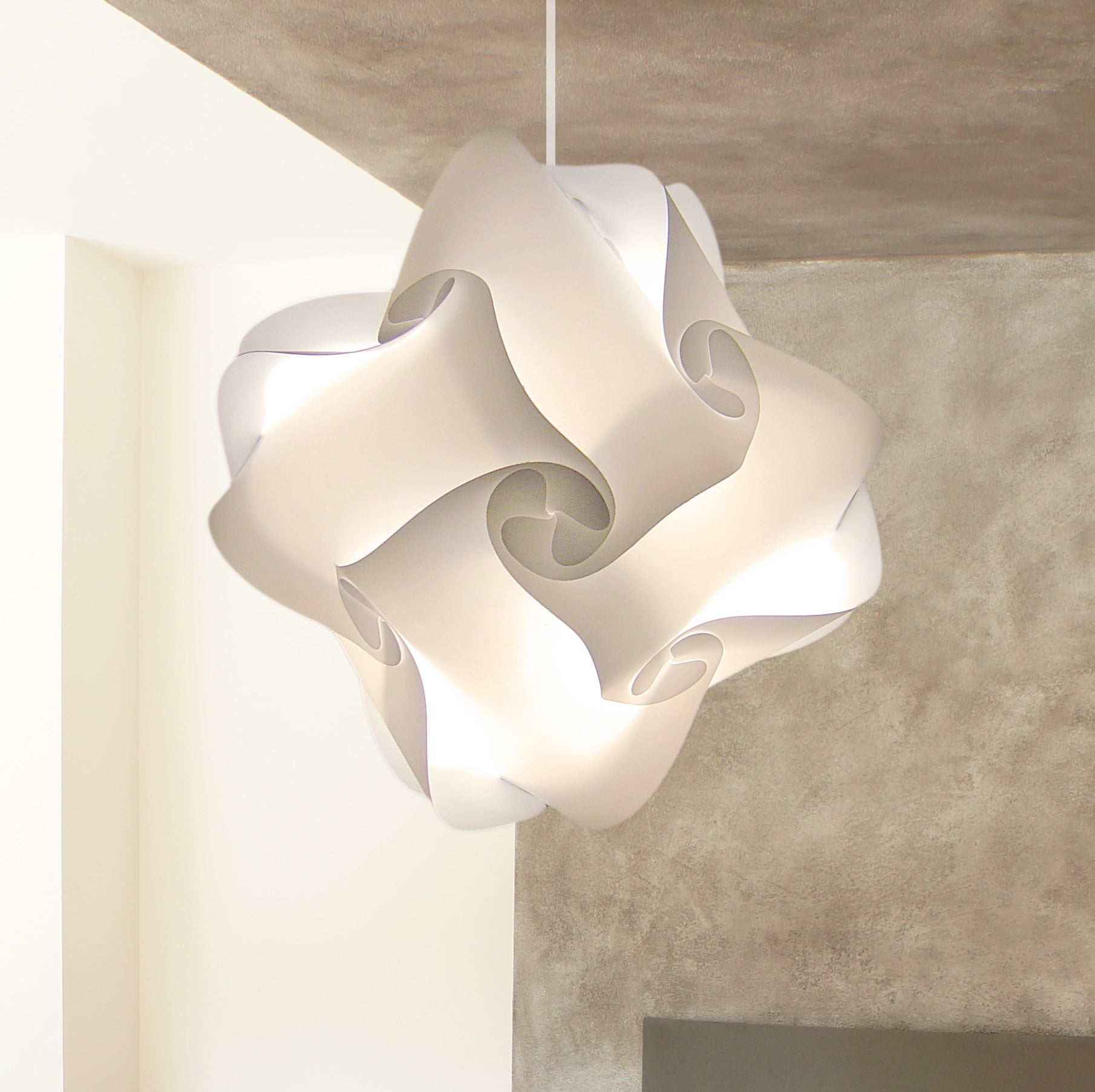 White artfully designed modern ceiling lampshade with intricate curves and folds, providing soft diffused lighting for a stylish home interior.