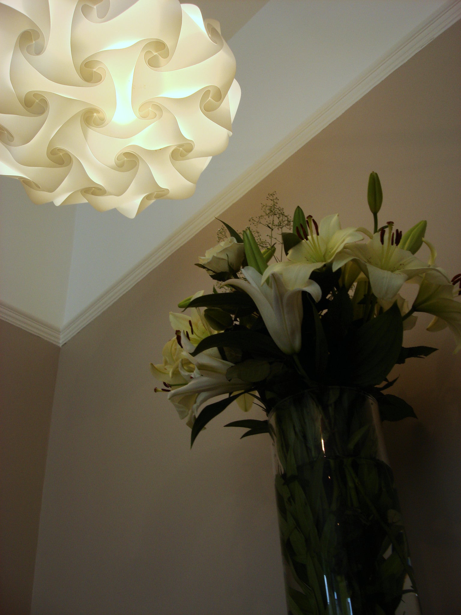 Modern white flower-shaped lampshade with lush green floral arrangement in vase below