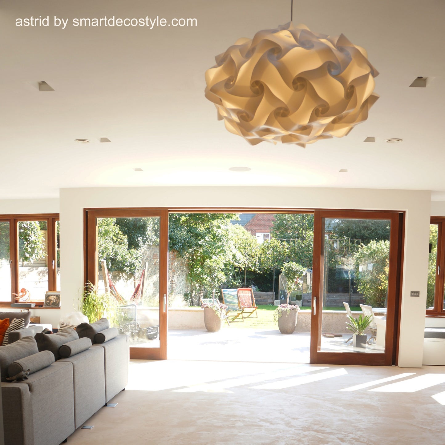 Elegant modern light fixture in minimalist interior with floor-to-ceiling windows overlooking a garden