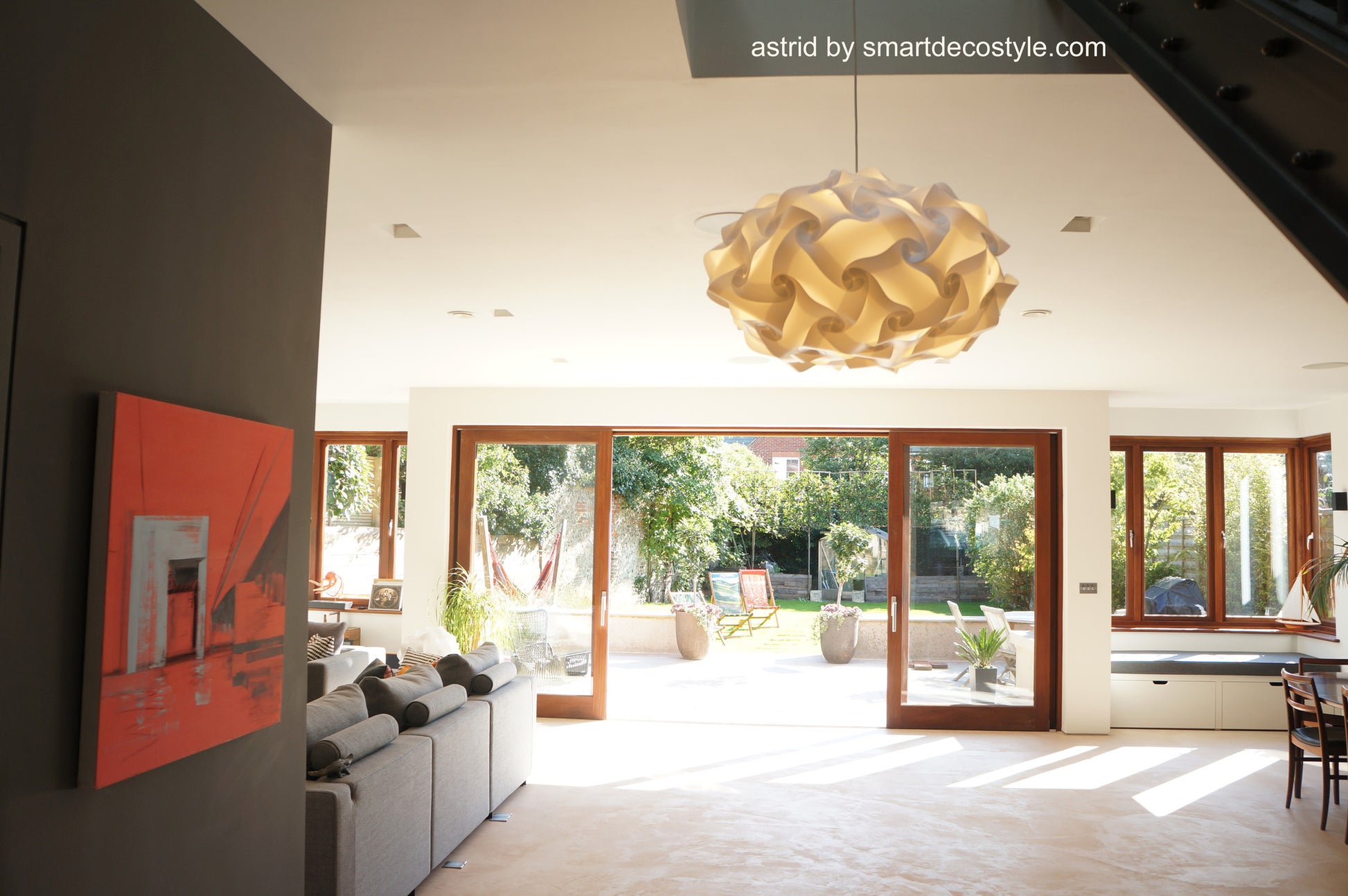 Stylish natural linen lampshade suspended from ceiling in chic home interior with large windows overlooking outdoor garden