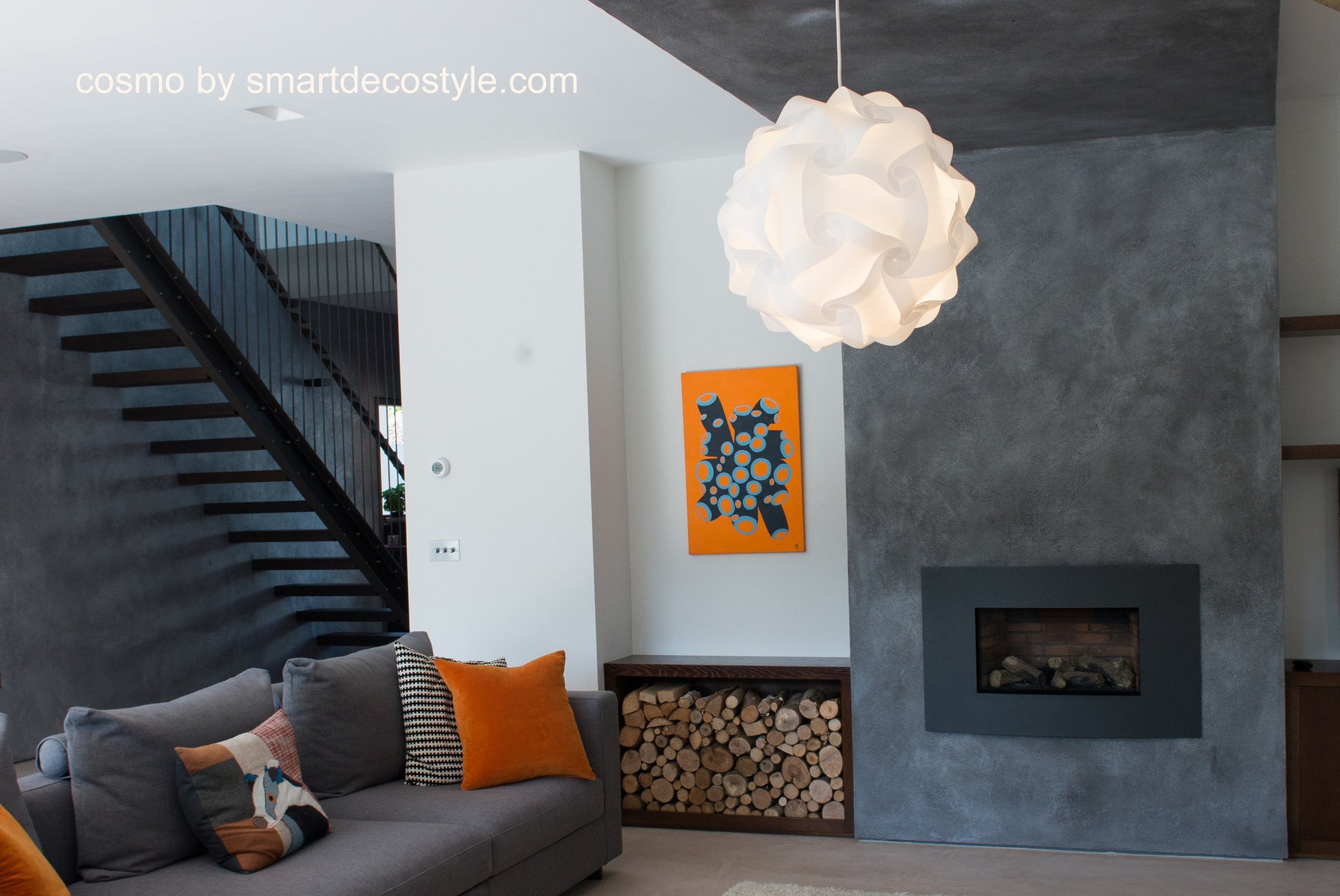 Stylish white pendant lamp in modern living room with gray and orange decor elements, firewood storage, and abstract wall art.
