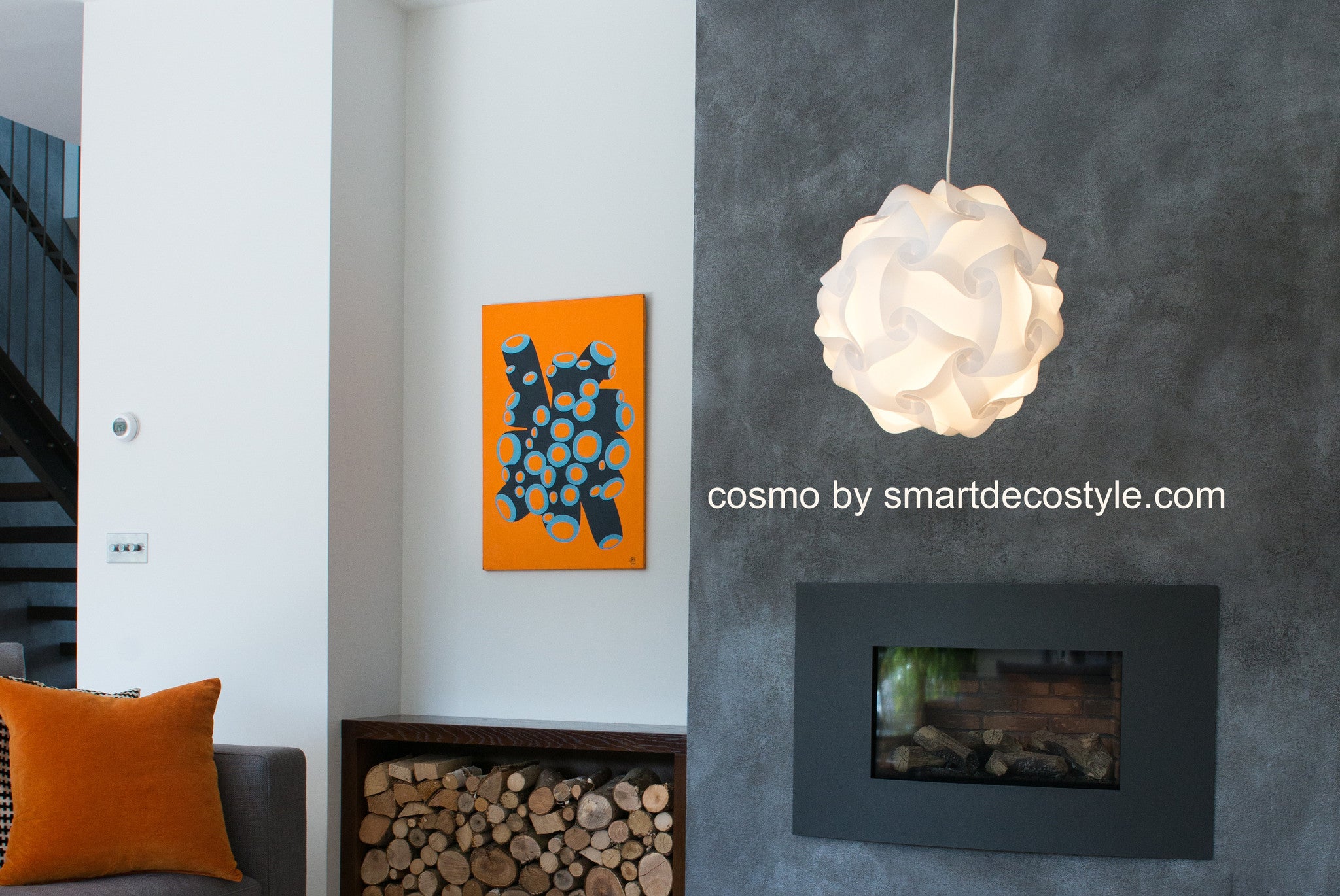 Modern white pendant light shade with a stylized floral design, displayed alongside an abstract orange and blue wall art piece in a contemporary interior setting.
