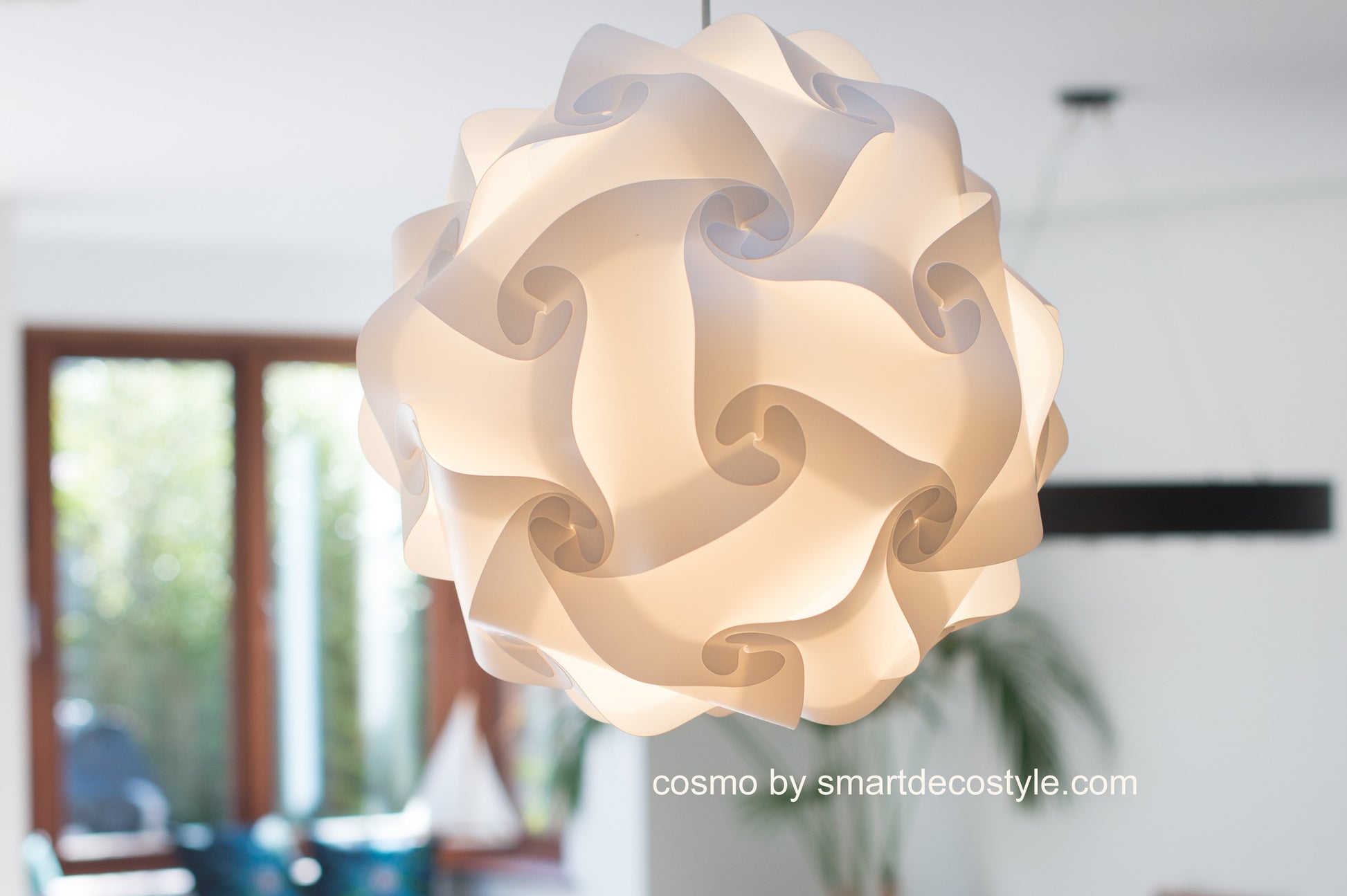Elegant white paper lampshade with intricate folds and curves, suspended from the ceiling, creating a soft, ambient glow in the room.