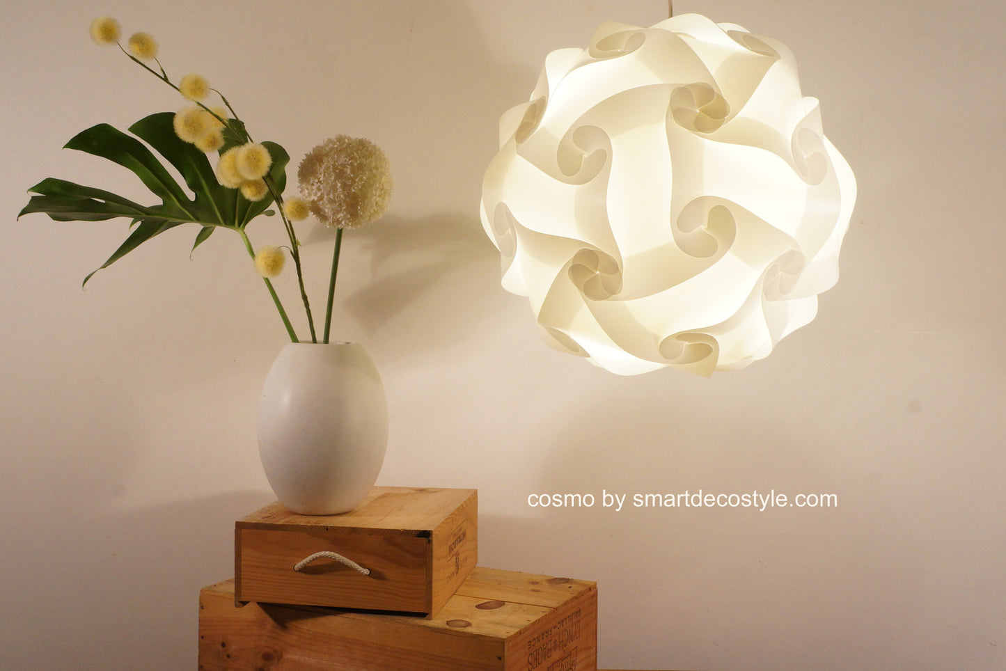 Unique white Cosmo pendant light shade on wooden crates with orchid flowers in a vase, decorative lighting solution for modern interiors.