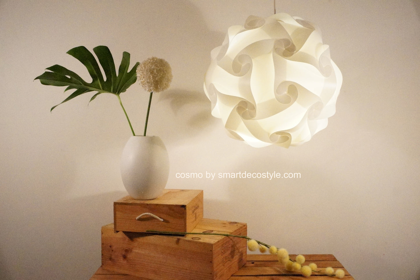 Stylish Cosmo Light Shade on display with tropical leaf, wooden crates, and decorative objects creating a chic home interior setting.