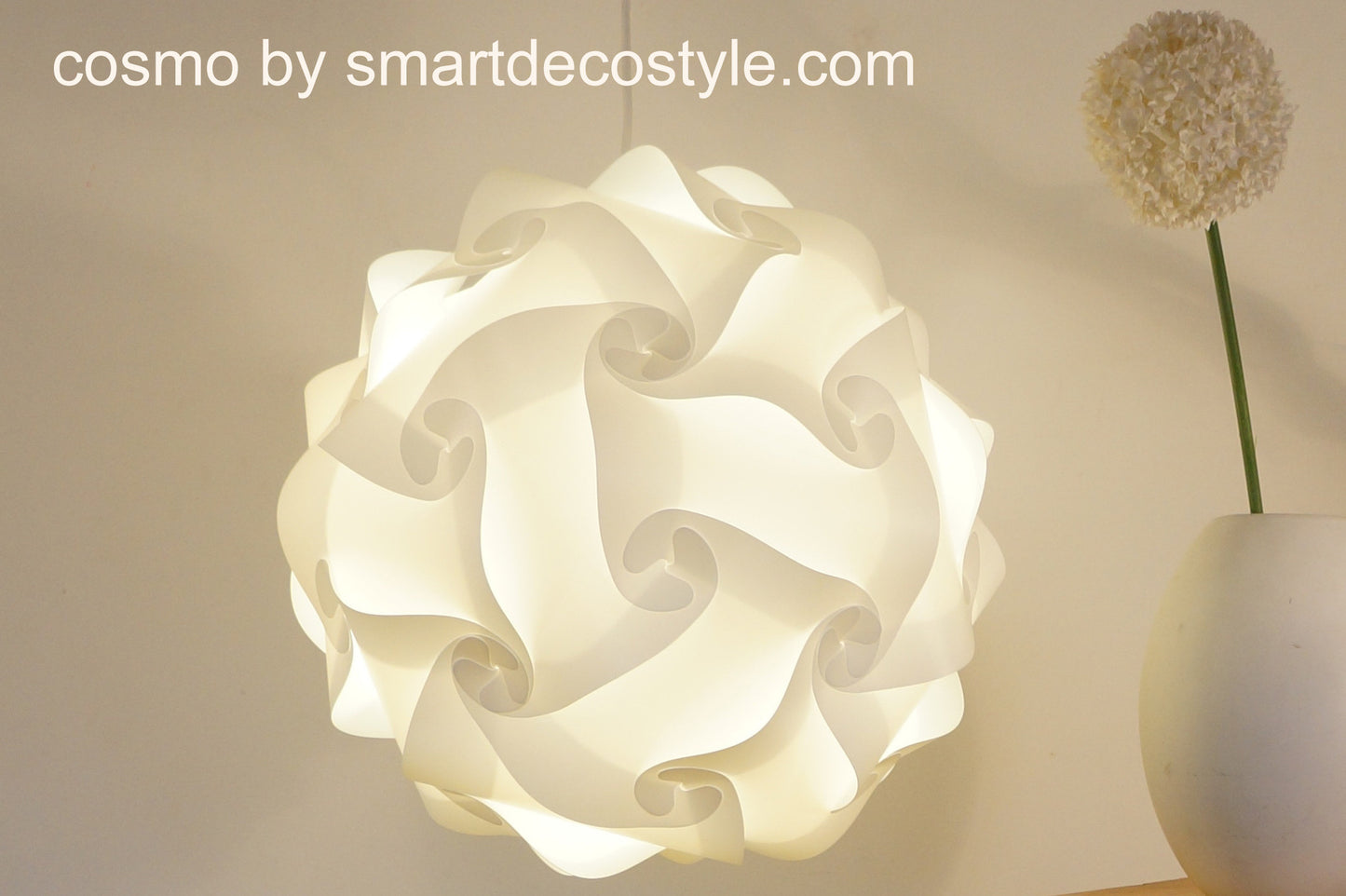 Elegant white paper lantern lamp shade with intricate swirling design, displayed on a minimalist background with a dried flower stem.