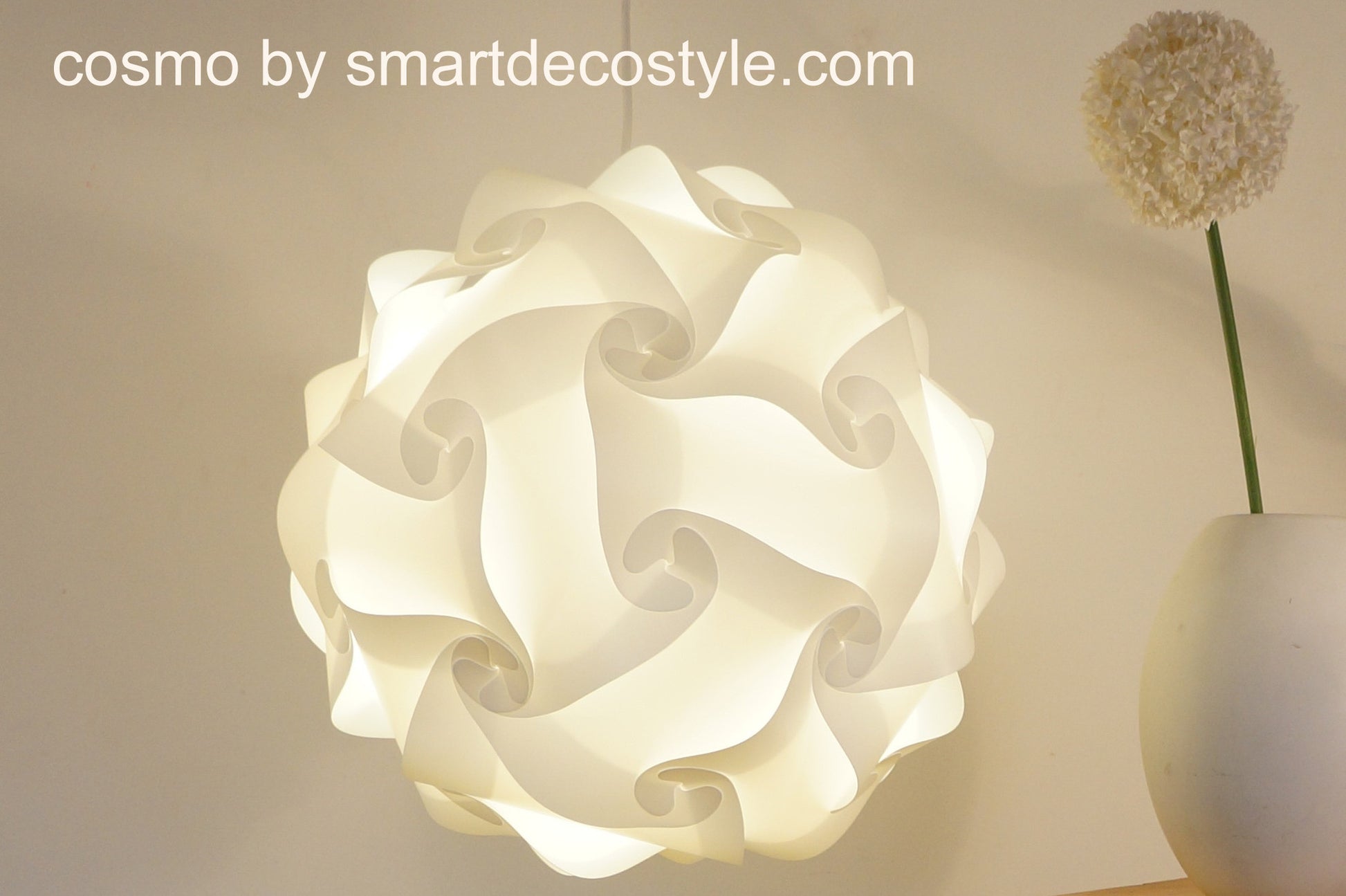 Elegant white paper lantern lamp shade with intricate swirling design, displayed on a minimalist background with a dried flower stem.