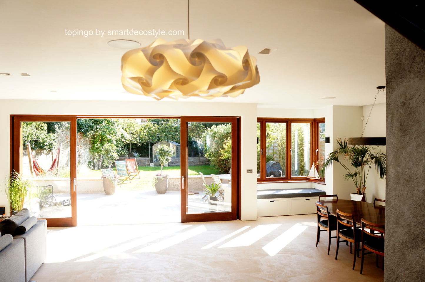 Elegant light fixture over cozy indoor seating area with large windows overlooking a lush garden in this modern home interior.