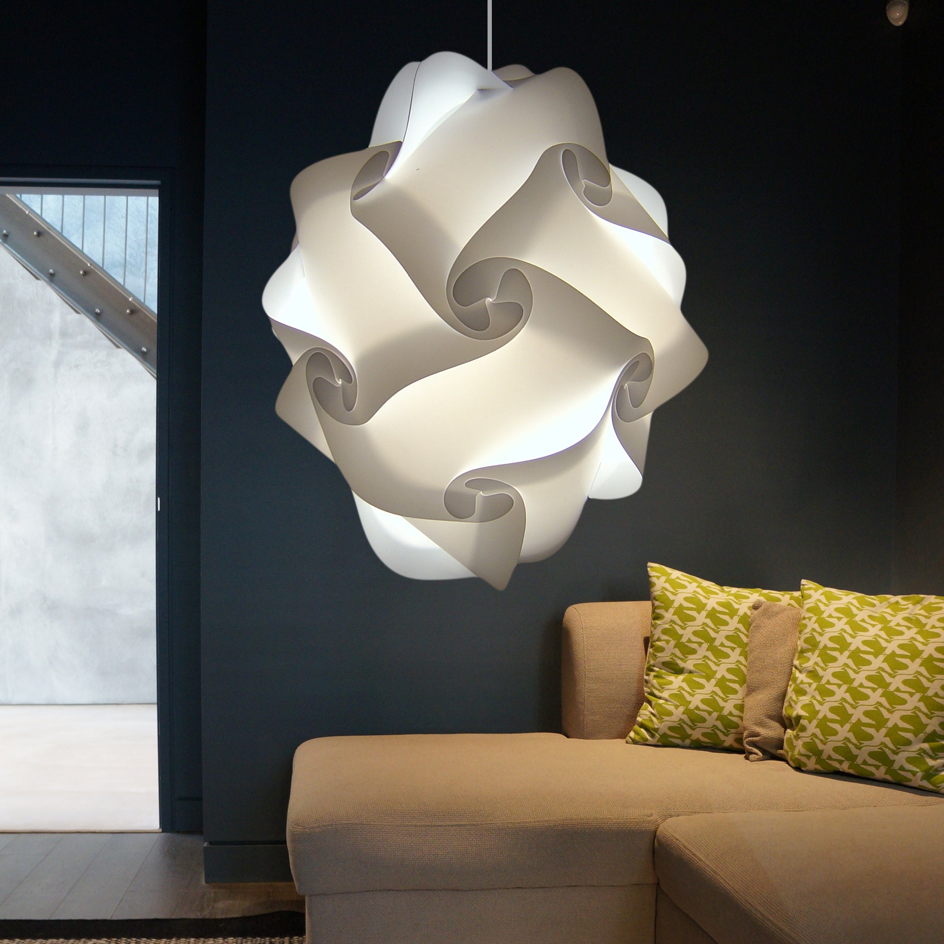 Sculptural white lamp shade suspended from ceiling, illuminating modern living room with patterned sofa cushions and glass door.