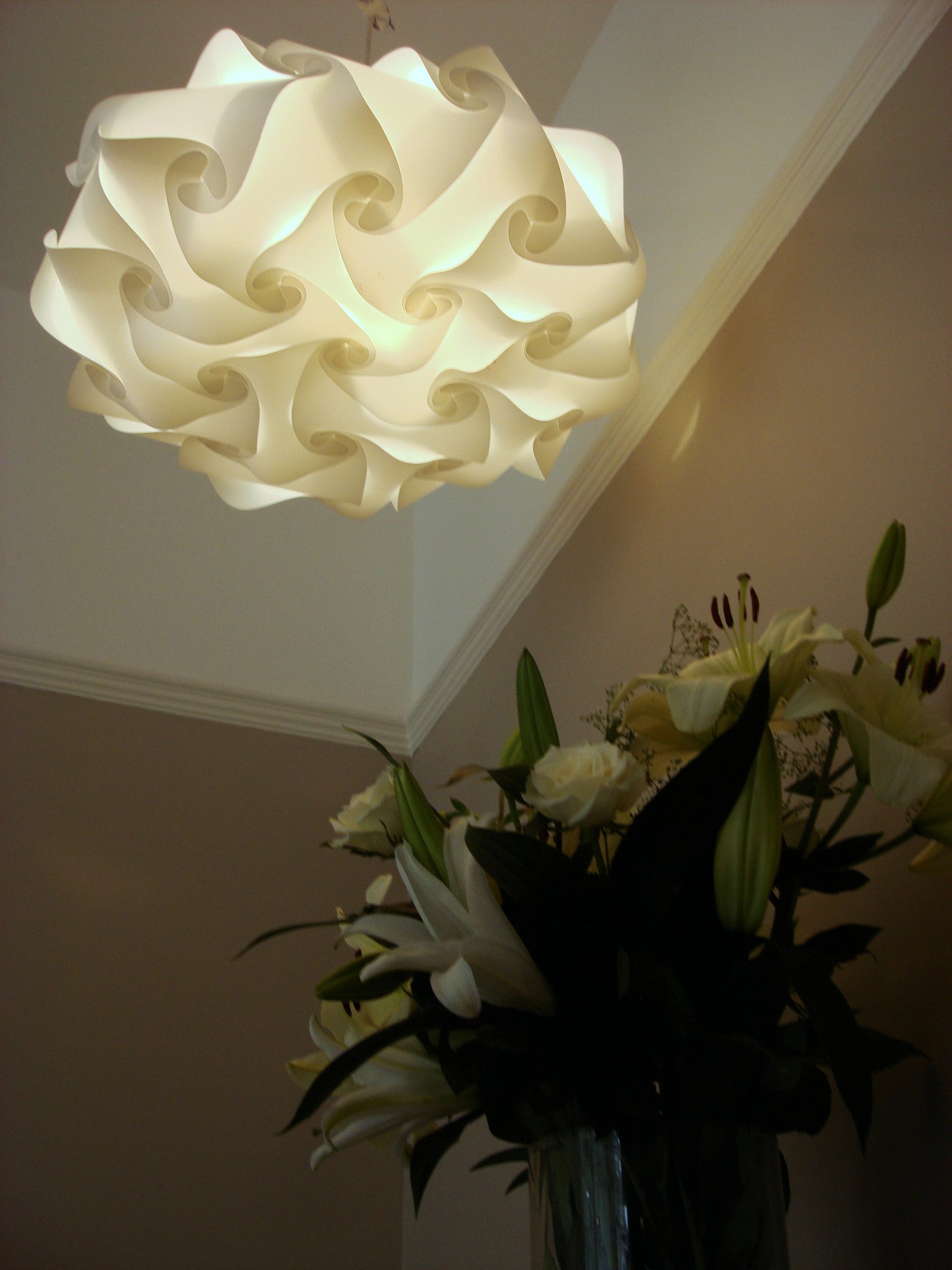 Elegant white swirl lamp shade suspended above a vase of fresh flowers in a cozy interior setting.