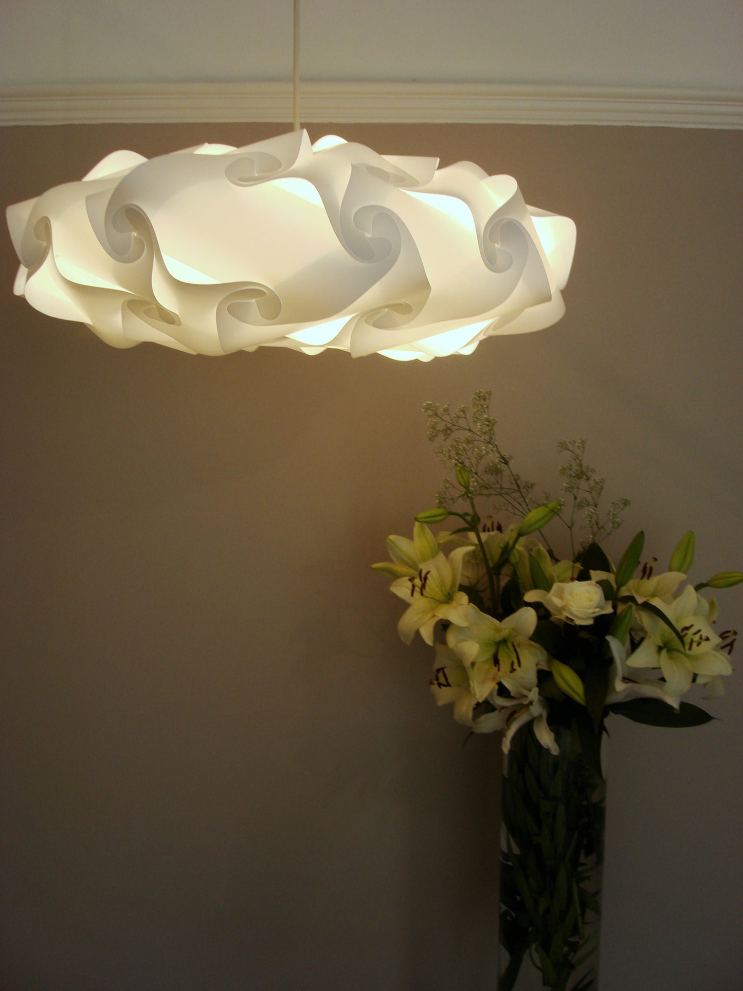 Elegant floral-inspired white lampshade suspending above a vase of vibrant flowers, creating a warm, inviting ambiance.