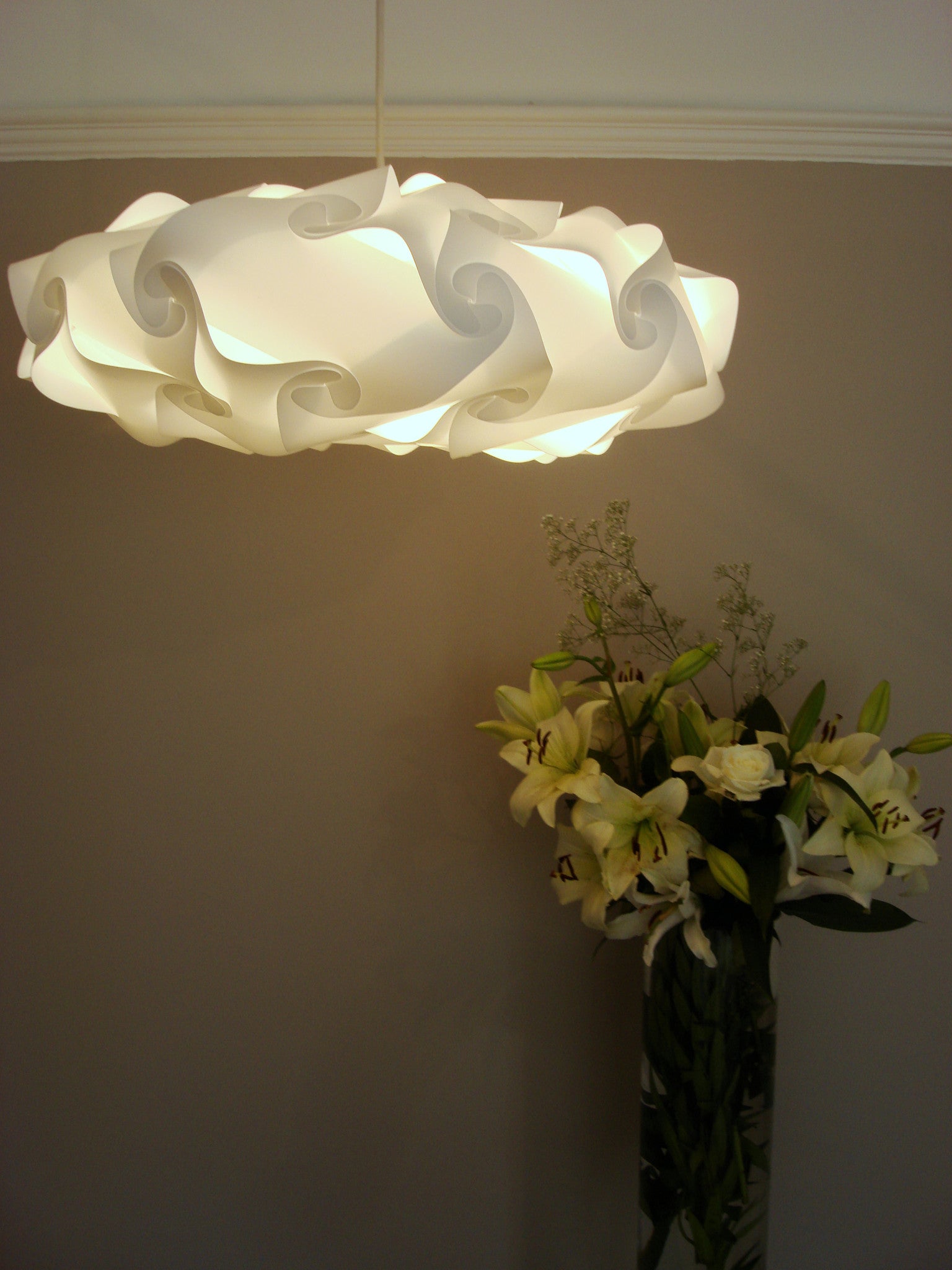 Elegant floral-inspired white lampshade suspending above a vase of vibrant flowers, creating a warm, inviting ambiance.