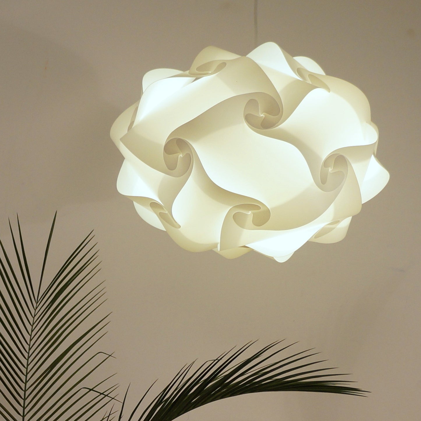 Elegant white swirl-shaped ceiling light fixture amid lush green palm fronds, creating a serene and modern ambiance.