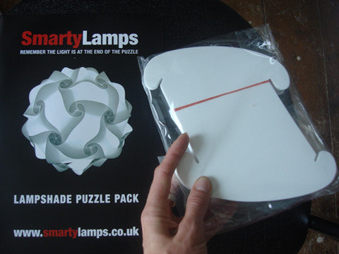 White modern lampshade puzzle pieces in a clear plastic bag, with the Smartylamps brand name and logo visible on the packaging. The image showcases the product's customizable and DIY nature, allowing users to build their own lampshades from the included pieces.