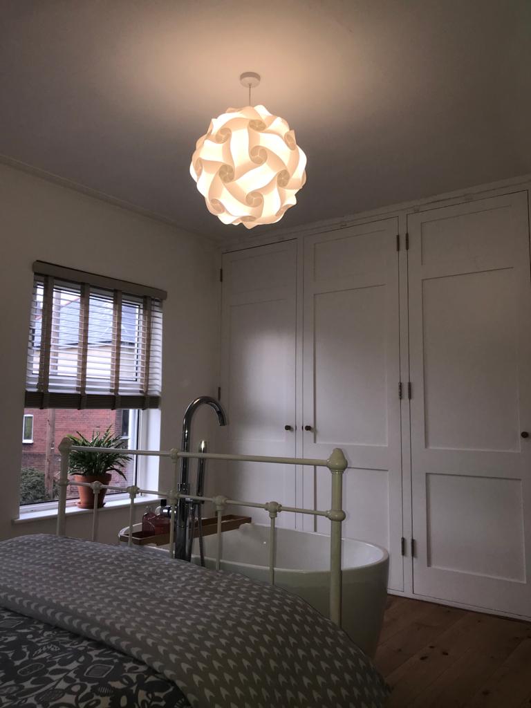 Modern white geometric pendant lamp hanging in a cozy bedroom with gray furnishings and wooden flooring.
