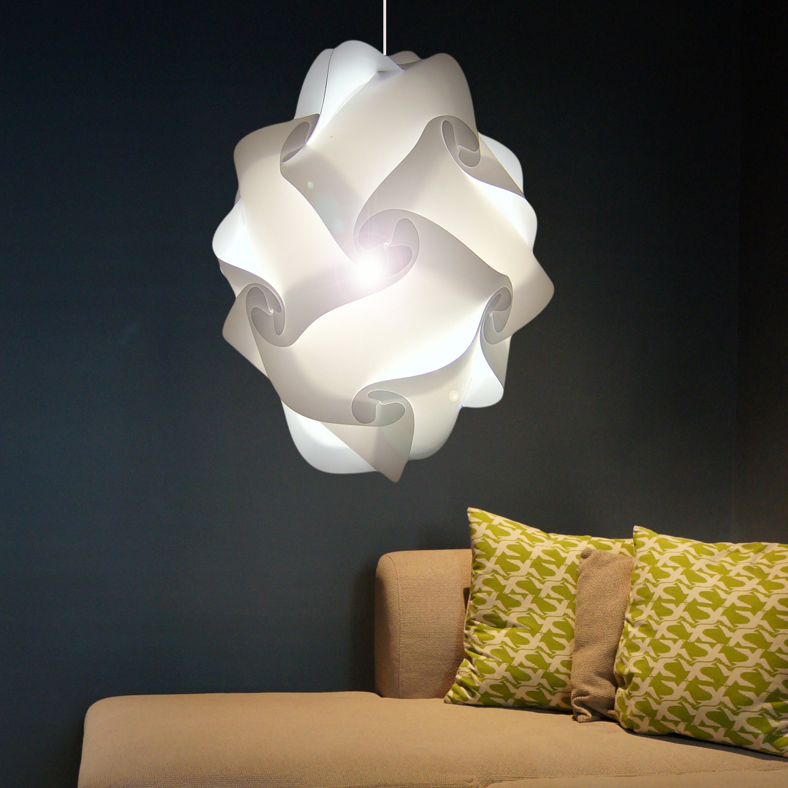 Beautiful white swirl pendant lamp with intricate design, illuminating a cozy living room with patterned throw pillows on a beige couch against a dark background.