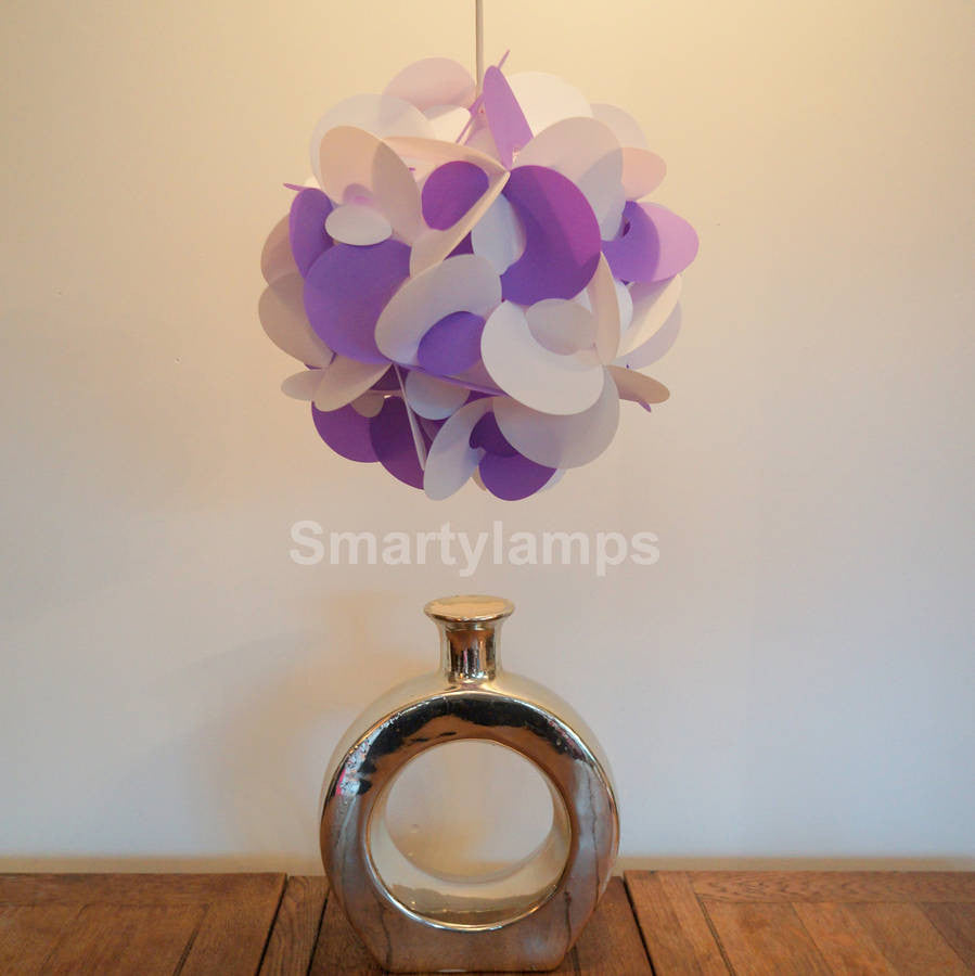 Curved purple and white decorative lamp shade hanging above a shiny metallic vase on a wooden table